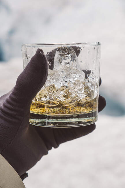 Hand holding glass of whiskey with ice — Stock Photo