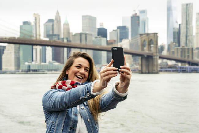 Atractiva mujer usando su teléfono inteligente con el horizonte de Nueva York en el fondo - foto de stock