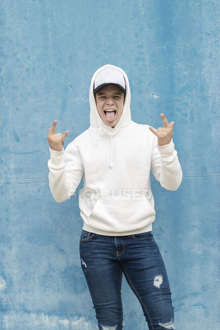 Portrait of a young male wearing hooded shirt while leaning on a blue wall and gesturing — Stock Photo