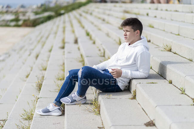 Вид сбоку на молодого человека, сидящего на открытой лестнице, отводящего взгляд — стоковое фото