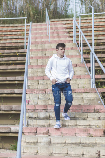 Jovem adolescente do sexo masculino descendo escadas mãos no bolso enquanto olha para longe — Fotografia de Stock
