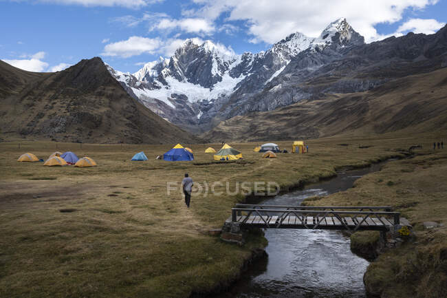 Una persona caminando hacia las tiendas de campaña de un campamento en la Cordillera Huayhuash - foto de stock