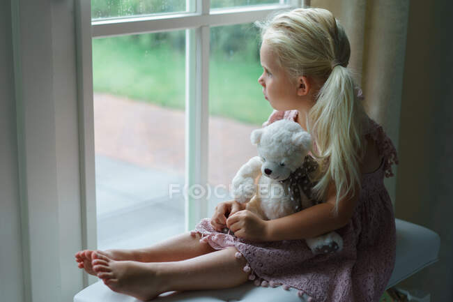 Petite fille regardant tristement par la fenêtre regarder la pluie. — Photo de stock