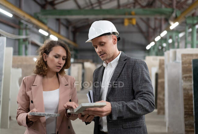 Adult female client in jacket exploring samples of stone with help of elegant supervisor of stone company manufacture — Stock Photo