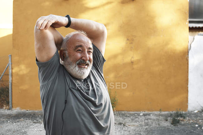 Un anciano estira el brazo con la cara dolorida - foto de stock