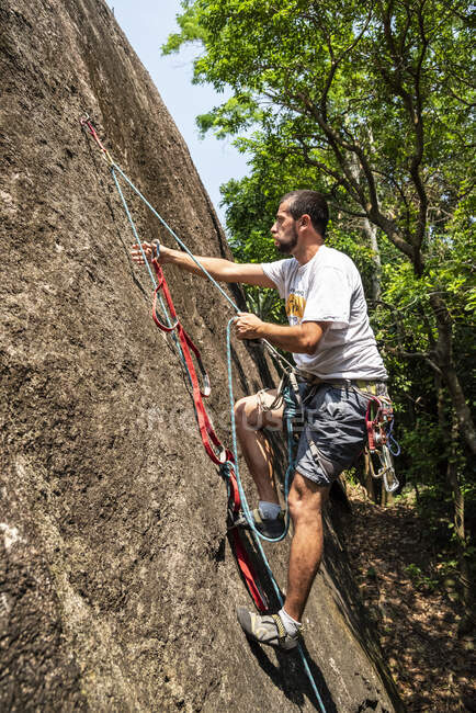 Vista all'uomo arrampicata su parete rocciosa nella foresta pluviale — Foto stock