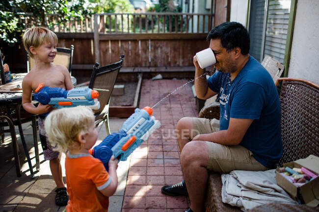 Hermanos disparando armas de agua al tío mientras bebía café - foto de stock