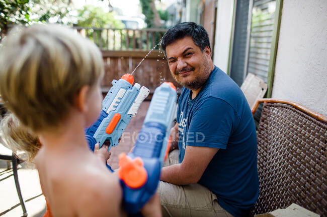 Des neveux tirent des pistolets à eau sur l'oncle dans la cour avant — Photo de stock