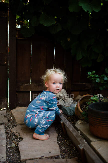 Ragazzo di due anni in pigiama accovacciato nel cortile anteriore sotto l'uva — Foto stock