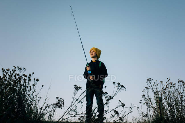 Young boy happily fishing at sunset alone — Stock Photo
