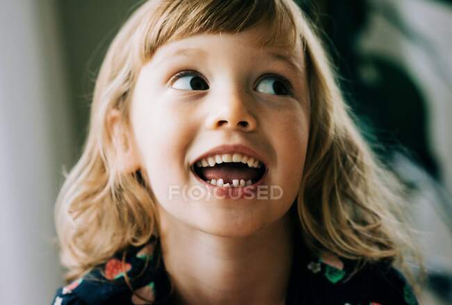Молода дівчинка посміхається, показуючи свій хиткий зуб, який виглядає щасливим. — стокове фото