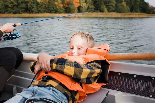 Young boy sat relaxing on a boat whilst out on a boat fishing — Stock Photo