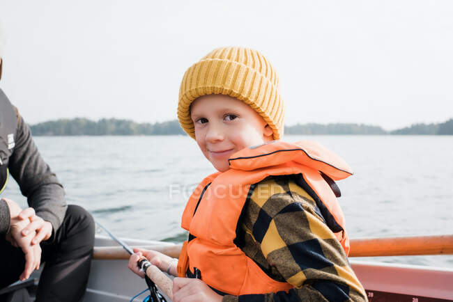 Young boy sat on a boat smiling whilst fishing with his family — Stock Photo