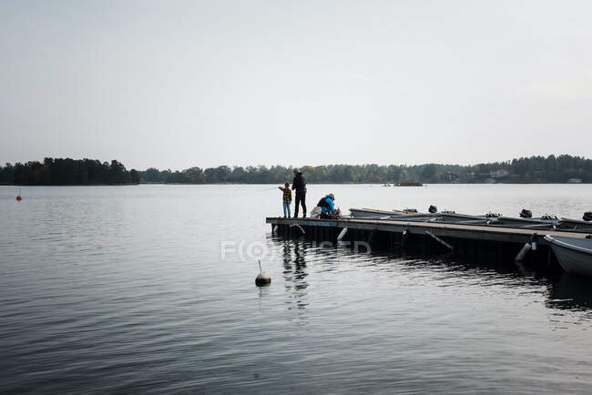 Niño pescando en el extremo de un muelle con su padre y amigo - foto de stock