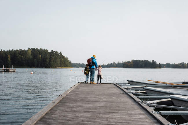Padre y sus hijos pesca felizmente en el extremo de un muelle juntos - foto de stock