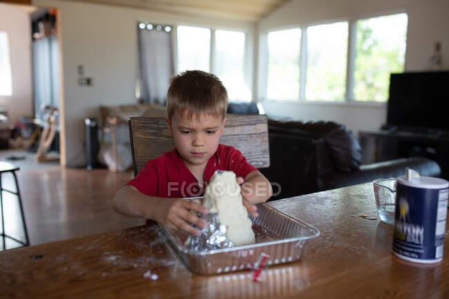 Menino fazendo vulcão de barro na mesa da cozinha — Fotografia de Stock