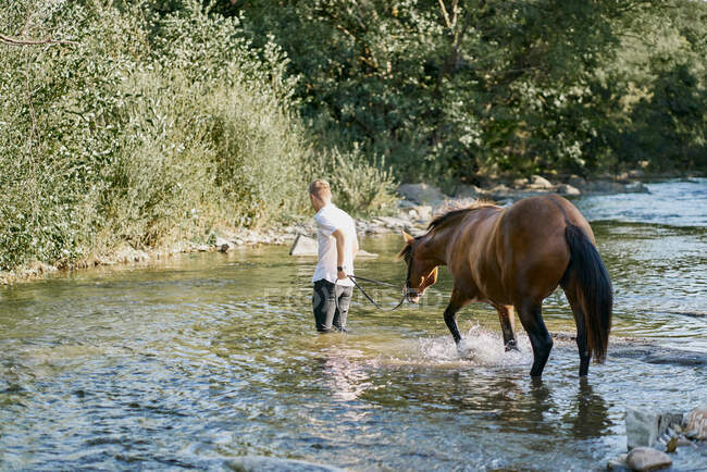 Retrato de um jovem loiro montando um cavalo sobre um rio — Fotografia de Stock