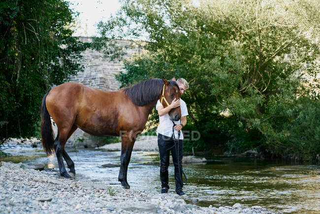 Portrait d'un jeune homme blond chevauchant un cheval sur une rivière — Photo de stock