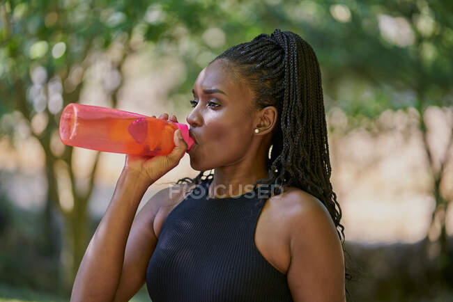 Портрет красивой черной женщины, пьющей из бутылки с водой — стоковое фото
