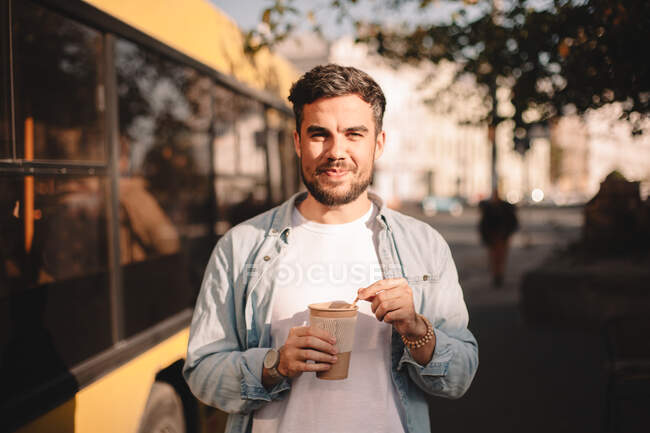 Happy man holding cup of coffee while standing on street during summer — Stock Photo
