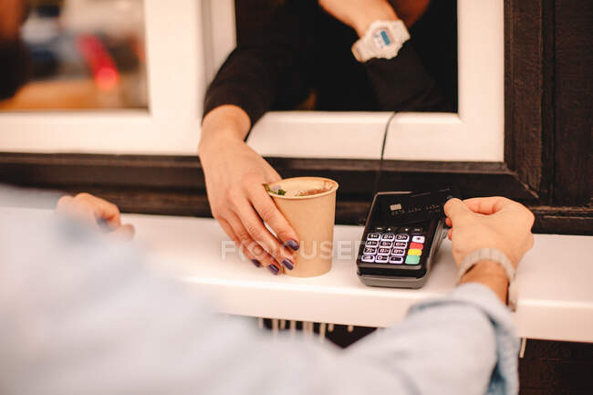 Imagen recortada del cliente haciendo el pago con tarjeta de crédito comprando café en la cafetería - foto de stock