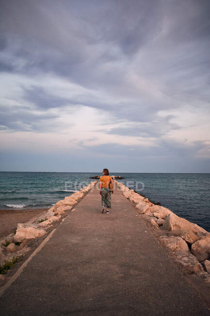 Donna di mezza età cammina su una passerella sulla costa — Foto stock