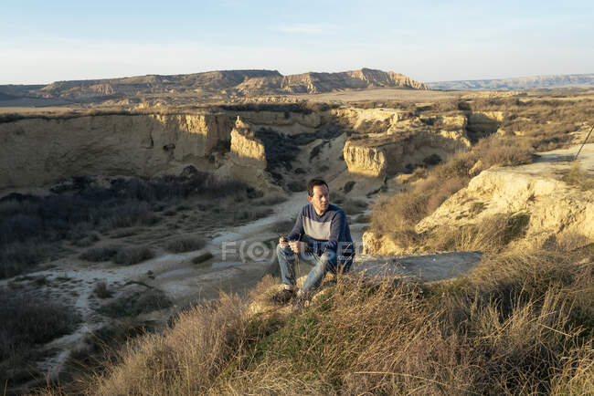 Vista laterale di un uomo rilassato seduto sulla cima di un canyon del deserto mentre distoglie lo sguardo — Foto stock