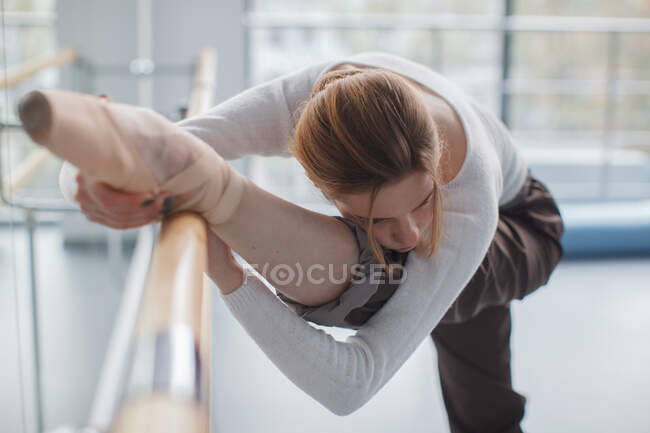 Belle jeune ballerine étirant ses jambes près du bar en classe de chorégraphie — Photo de stock