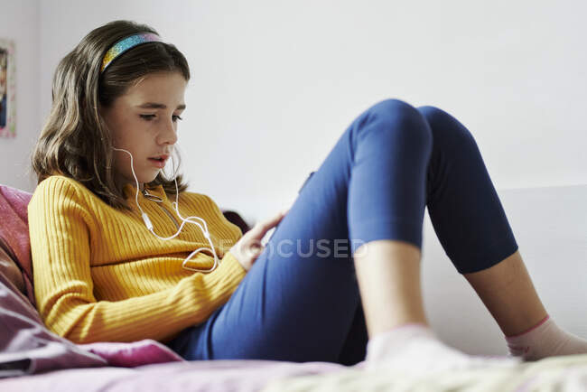 Mädchen liegt auf ihrem Bett und schaut auf ein Tablet und trägt Kopfhörer — Stockfoto