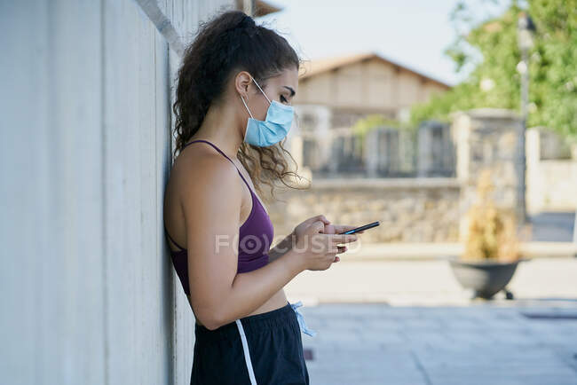 Mulher de sportswear usando uma máscara médica olhando para um smartphone — Fotografia de Stock