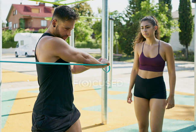 Young man and woman practicing calisthenics with an elastic band — Stock Photo