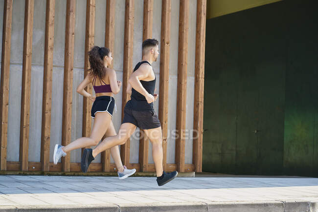 Young man and woman running on the street on sunny day — Stock Photo