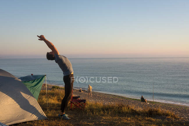 Adult man stretches in the morning in front of the tent — Stock Photo