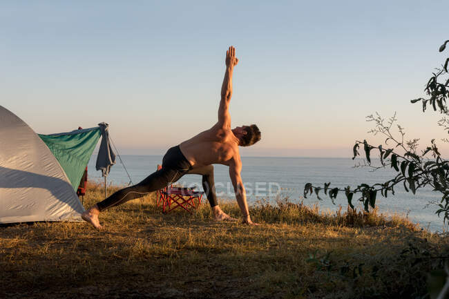 Дорослий чоловік робить фізичні вправи на сході сонця, перед наметом — стокове фото