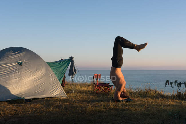 Hombre adulto hace yoga al amanecer, frente a la tienda junto al mar - foto de stock