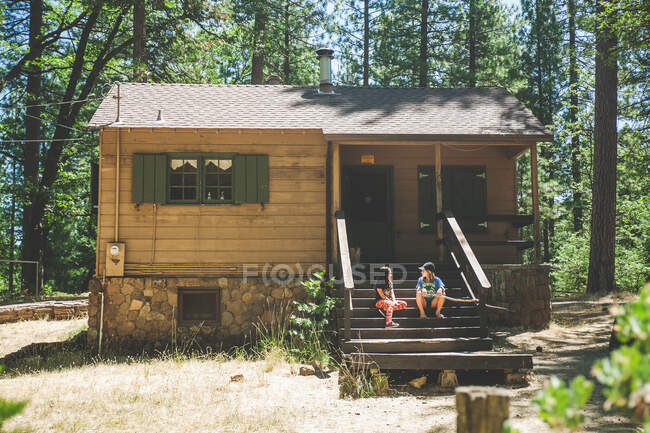 Children sitting on cabin porch in the woods — Stock Photo