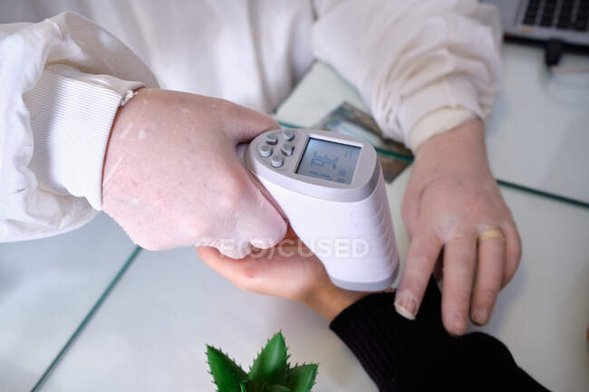 Mujer blanca usando medidor de temperatura con paciente durante el bloqueo - foto de stock