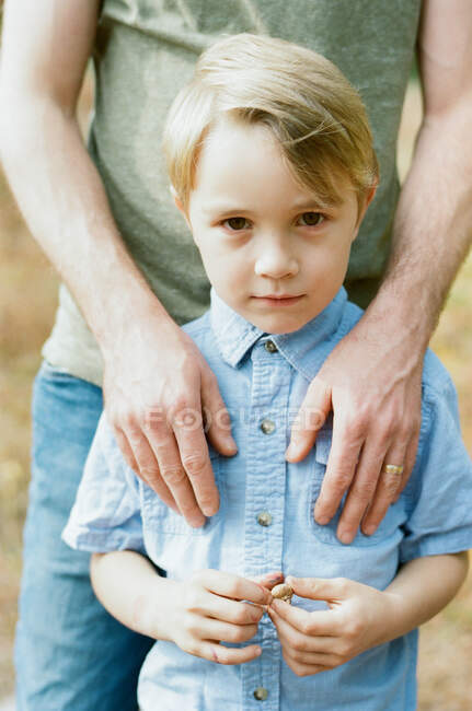 Petit garçon debout devant son père regardant dans la caméra — Photo de stock