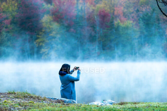 Woman taking photo with phone of the fog and New England fall foliage. — Stock Photo