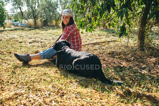 Joven campesina descansa en el suelo junto a su perro - foto de stock