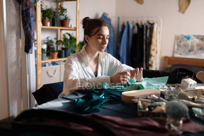 Стильная брюнетка, работающая в домашней ателье с небольшим бизнесом, пока шьет одежду за столом — стоковое фото