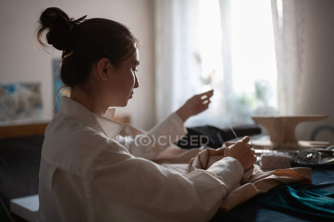 Back view of focused brunette owning small business of sewing clothes and making new garment in home studio — Stock Photo