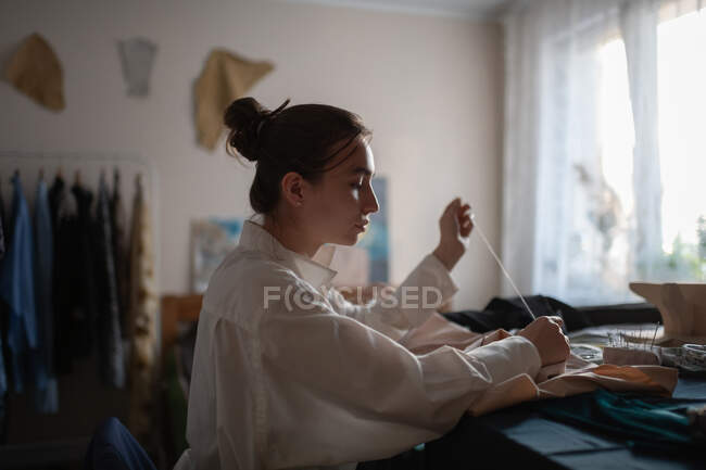 Seitenansicht einer lässigen Frau, die im Atelier zu Hause ist und Kleidung herstellt — Stockfoto
