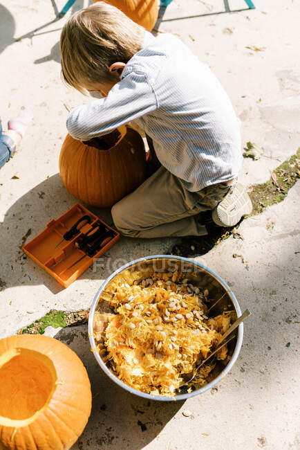 Um rapazinho a escavar a abóbora para o Dia das Bruxas no pátio — Fotografia de Stock