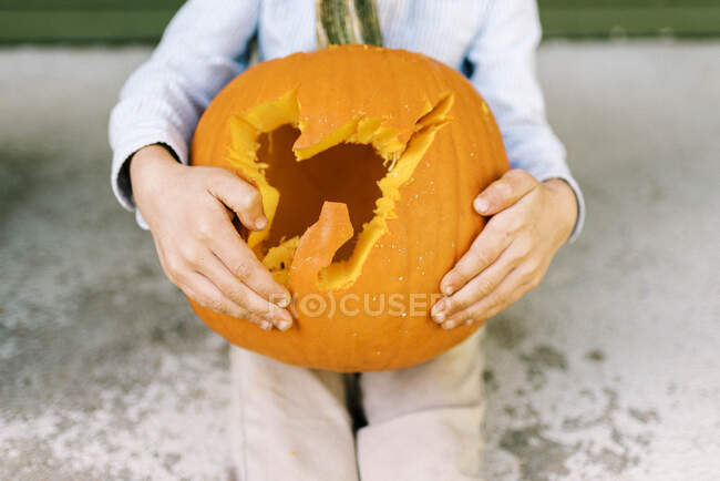 Petit garçon assis sur son porche montrant la citrouille sculptée d'Halloween — Photo de stock