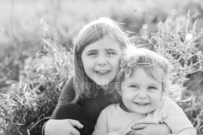Dos hermanas sonriendo juntas en un día ventoso afuera - foto de stock