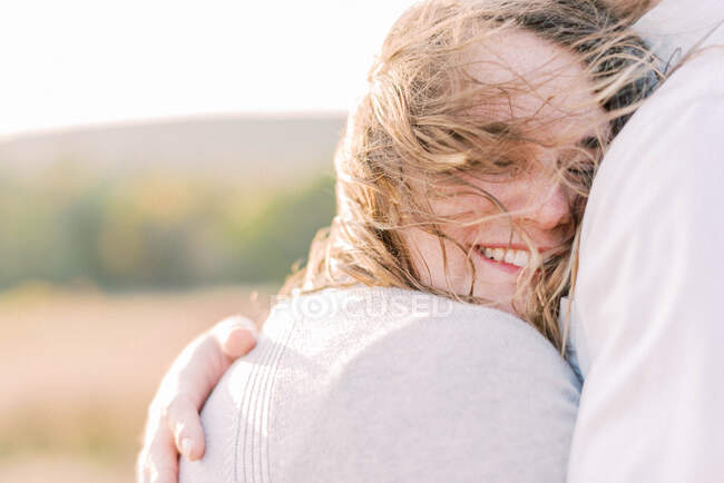 A beautiful woman being held by her husband on a windy day — Stock Photo