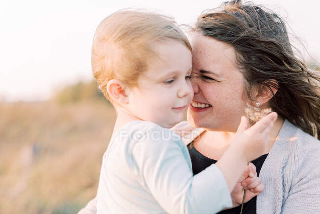 Una niña feliz y cariñosa sostenida por su madre en un día ventoso - foto de stock