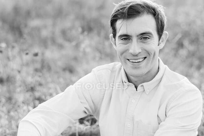 Un joven sentado en la hierba y sonriendo - foto de stock