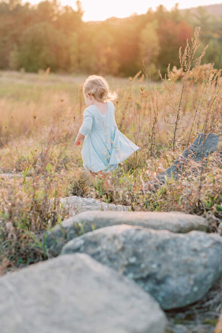 Маленькая девочка бежит через большие камни в поле на солнце — стоковое фото